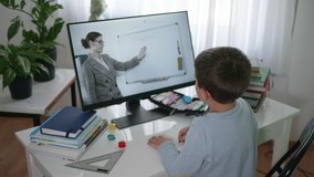 remote education, male school child learns lessons online using video broadcasting and modern technologies, looks at monitor screen and does homework, learning online