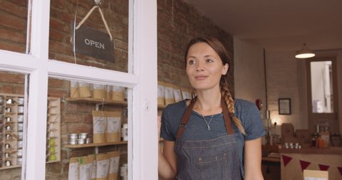 Portrait of pretty female retail store owner entrepreneur opening door with open sign and looking outside