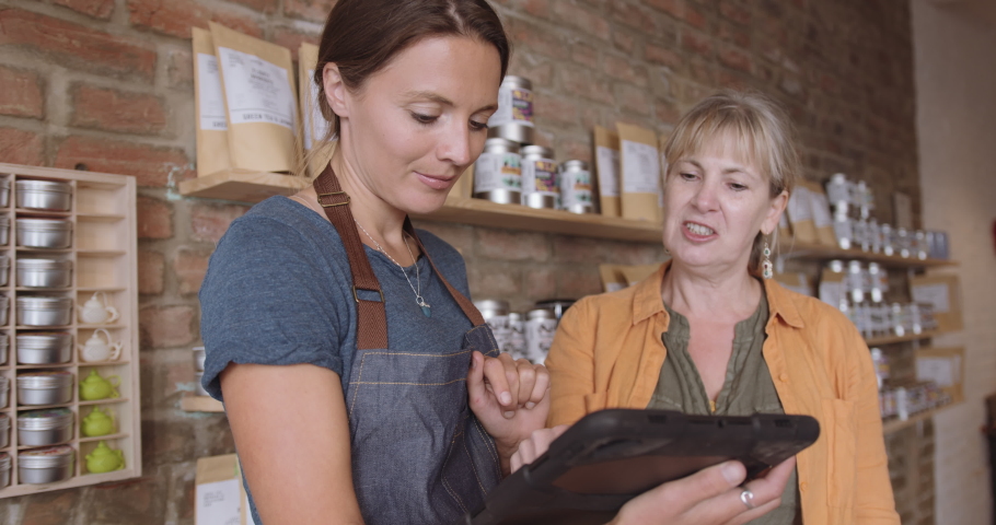 Female retail store owner advising customer in shop using digital tablet | Shutterstock HD Video #1057278736