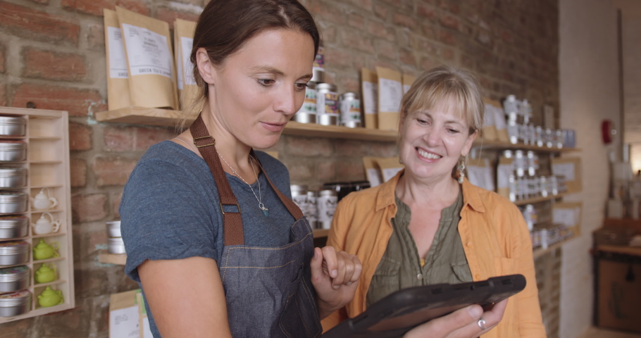 Female retail store owner advising customer in shop using digital tablet Royalty-Free Stock Footage #1057278736