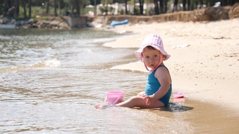 Baby child toddler girl plays on shallow waterline sand beach of Aegean sea in Greece
