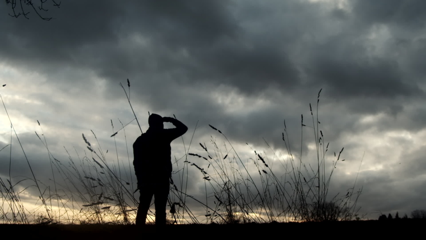 Hiker looks over field at golden hour with dramatic clouds overhead