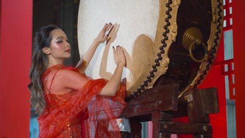 Beautiful Asian woman wearing a traditional red Chinese dress beats the large drum to celebrate the Chinese new Year - static slow motion