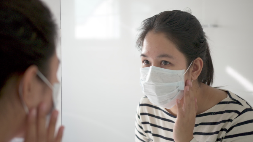Young adult asian woman worry unhappy with skin acne or pimples from wearing face mask showing swollen, spot, scar, skin allergy on chin and cheek in mirror in maskne covid-19 social distance concept. Royalty-Free Stock Footage #1057289143