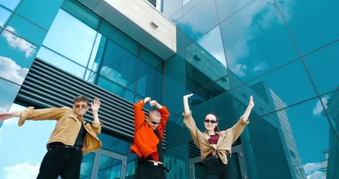 Model teen friends people in sunglasses, stylish red shirts dance having fun outdoors near city glass mirrored building, blue sky reflection, three  young persons bodies crazy dancing moving to music