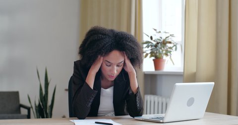 Tired exhausted Afro woman bored of routine work study in office at home with laptop, loses energy, lays head on hands on table, falls asleep long day at workplace, girl feeling sluggish unhealthy