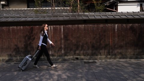 European tourist walk with trolley case against wooden fence, old Kyoto street. Slow motion shot, traveler woman have short time to explore famous Hanamikoji Street at Gion district