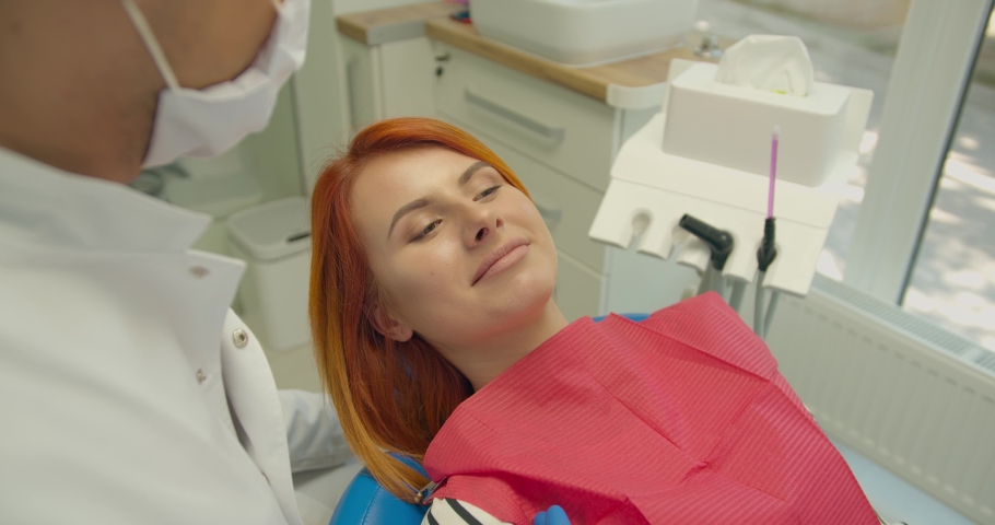 Confident smiling young adult european woman looking at camera standing at dental office. Happy millennial casual red-haired lady with white teeth pretty face posing for close up portrait indoors. Royalty-Free Stock Footage #1057299157