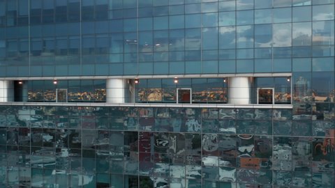 Colorful Mexico city is reflecting in the glass windows of modern skyscraper with town on motion background. 4K drone. Cinematic aerial close up of modern glass building in Mexico business district