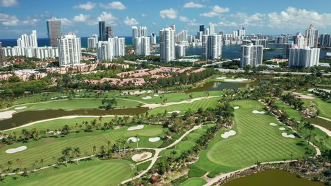 4K cinematic drone panorama view Miami Sunny Isles skyline. Scenic prestige green golf field with tropical palm trees. Modern waterfront buildings with ocean view, Florida, USA. Sunny summer day