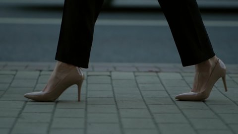 female feet in high-heels shoes, closeup, woman is walking on city street
