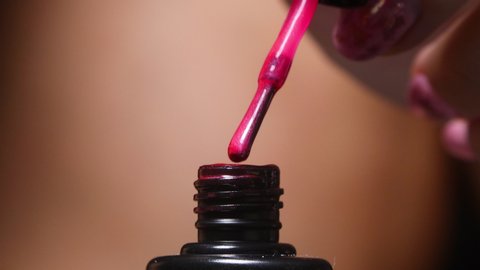Taking out nail brush from bottle with nail polish and smear to remove surplus of nail polish. Macro close up 