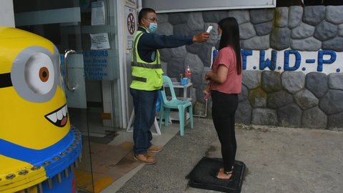 La Trinidad, Benguet, Philippines - July 22, 2020: A Filipina woman steps onto a rug sprayed with disinfectant and then have her temperature taken by a security guard before entering a building.