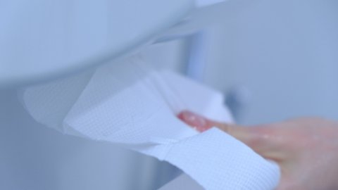 
woman hands pulling napkins from white plastic box in clinic toilet.