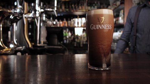 NIZHNY NOVGOROOD, RUSSIA, June 21, 2016 - Bartender puts a glass of cold dark Guinness on bar. Foam slowly settles. Bar background. High quality 4k footage