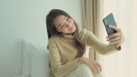 Smiling Japanese woman use phone and selfie happily on bed at home