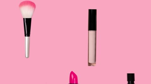 Different makeup accessories fly on trendy pastel pink background. Beauty animation. Cosmetic products. Make-up tools set concept. Lipstick, mascara, brush, perfume, nail Polish fall down. Skin care.