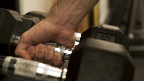 Dumbbells weights in a row. male athlete putting down dumbbells to rack, strength training equipment in gym. Muscle built bodybuilder. Closeup of hand grabbing and lifting kilograms at workout studio