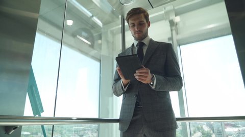 Businessman, young top manager goes to the top in the elevator and uses a screen tablet and rides in a panoramic Elevator in a office skyscraper.