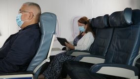 4K: Caucasian Female Airplane Passenger using a Digital Tablet wearing Face mask on plane journey. Air Travel. Tracking Shot. Stock Video Clip Footage