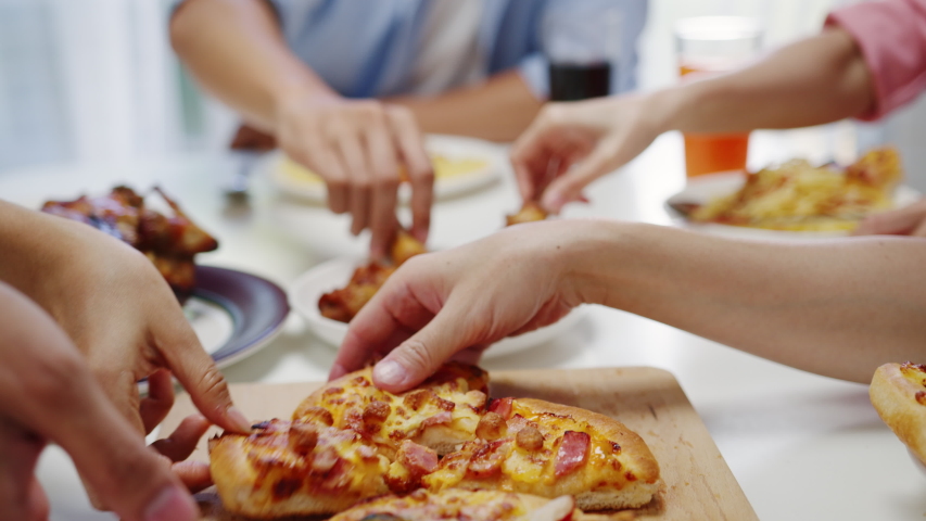 Close up shot of pizza on table, young friends group having lunch sitting around and picking up a portion at home. Asia family party eating food at dining table. Celebration holiday and togetherness. | Shutterstock HD Video #1057328527