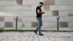 man with a mobile phone walks along the wall of a building on the street