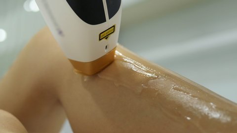 Beautician removes hair on beautiful female legs using a laser. Laser procedure at clinic