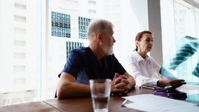 Woman doctor talking and holding in hands x-ray image during conference in hospital. Multi-ethnic group of physician of examine x-ray lungs of patient on background of window with MRI scans. - Powered by Shutterstock - Get 15% off with code: PIKWIZARD15