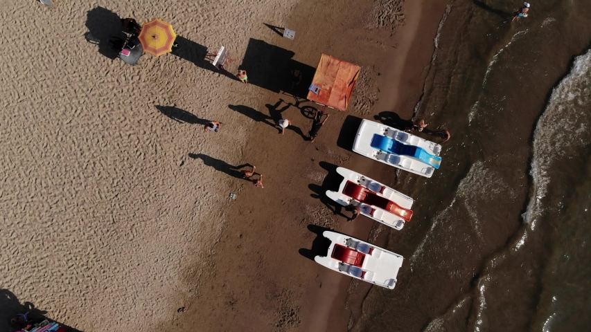 Aerial view of a person pushing the bicycle with fruits and vegetables during a hot summer day at the beach. Adriatic sea brown sand waves sunset pedal boat