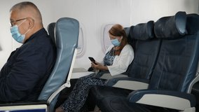 4K: Female Caucasian Airplane Passenger using a Phone and wearing Face mask on plane journey. Air Travel. Tracking Shot. Stock Video Clip Footage