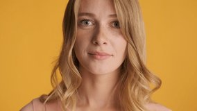 Pretty blond girl happily raising eyebrow looking on camera over yellow colorful background. Fooling around girl