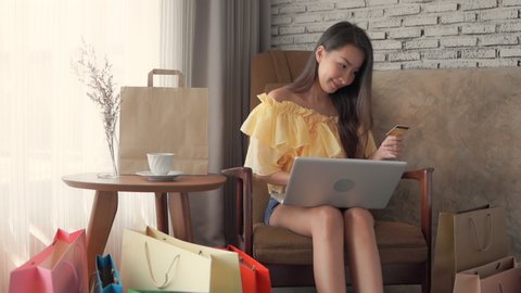 Young asian woman using her credit card to pay for her online shopping while in the comfort of her own house.