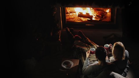Man and woman drink tea by the fireplace, good evening together, home comfort