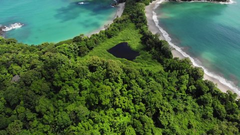 Aerial shot of tropical forest of National Park Manuel Antonio and Cathedral Point, Costa Rica. Sunny weather, clear blue green water. Flying backwards.