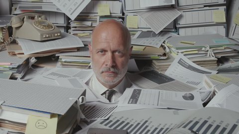 Stressed senior businessman in his messy office, he is overloaded with paperwork and screaming