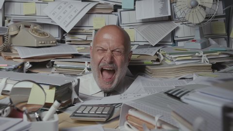 Stressed businessman overloaded with paperwork in the office, he is screaming and feeling desperate