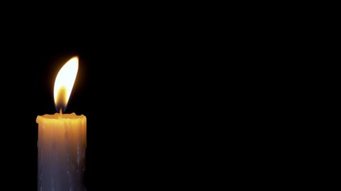 A single white candle burning.Isolated candle burning with dark background.White paraffin candle with yellow shades burns on a black background.Background or illustration of remembrance or celebration