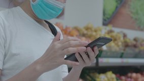 Close up woman wear surgical mask sliding smartPhone standing next to supermarket fruits shelf, wireless network 4g 5g technology, house wife scrolling phone, virus pandemic, shopping at grocery  - Powered by Shutterstock - Get 15% off with code: PIKWIZARD15