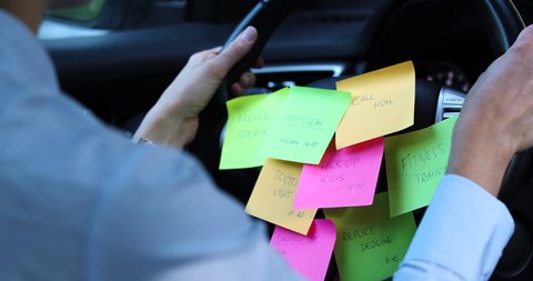 busy day schedule concept - woman driving car with to do list notes on the wheel