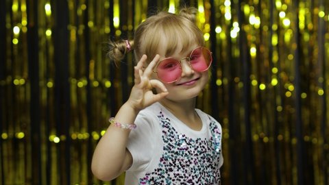 Cheerful glad child showing ok gesture and smiling at camera with optimistic satisfied expression, okay sign of approval. Little fun blonde kid teen teenager girl 4-5 years old in pink sunglasses