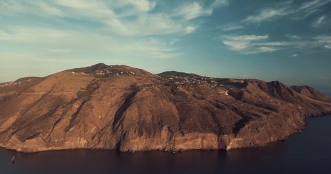 Drone panoramic aerial view of the vulcano island in the blue Mediterranean sea in Lipari, Sicily. Drone is flying backward from cliff to the blue sea showing crazy sunset colors