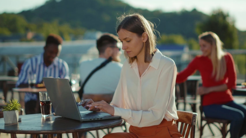 Serious beautiful young woman sitting at table with laptop in cafe working online typing internet online communication technology business outdoors slow motion Royalty-Free Stock Footage #1057358893