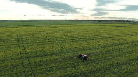 Tractor spraying fungicide in green field, tracking drone shot