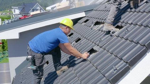 Roofer placing tiles in a house roof. Side view of construction work