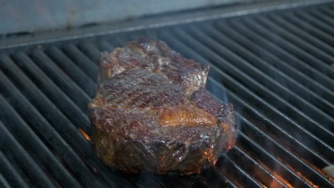 Close-up of flipping a juicy steak on the BBQ and brushing on sauce as the flames rise on the grill.