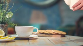 Woman's hand pouring tea from glass jug into a cup of tea. Breakfast concept. Lemon slices. Tea time. Super Slow Motion Shot of Pouring Tea into glass.