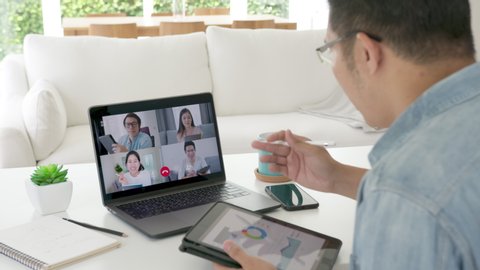 Zoom out the back view. businessman talking in a video conference.Asian team using laptop and tablet online meetings in a video calls.Working from home, Working remotely and Self isolation at home