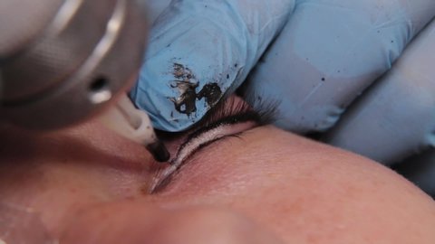A permanent makeup artist gets a tattoo on a woman's upper eyelids.