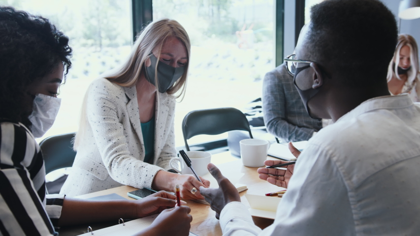 Office workplace with COVID-19 safety. Young multiethnic business people meeting at work wearing multi-use face masks.