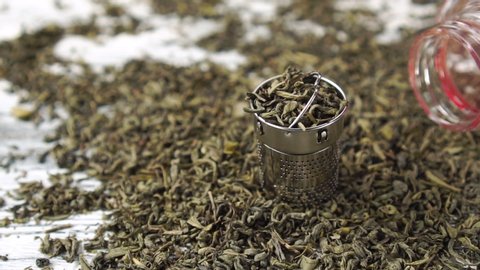 Green tea. Close-up of dried folded leaves falling into a stainless steel teapot basket. Slow motion. Dolly shot. Chinese traditional flavored drink
